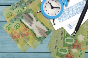 20 Canadian dollars bills and alarm clock with pen and envelopes. Tax season concept, payment deadline for credit or loan. Financial operations using postal service